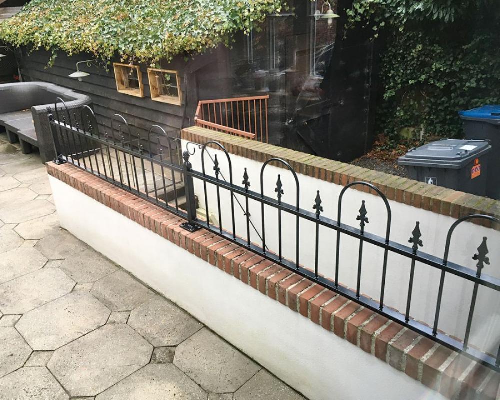 Gepoedercoat sierhekwerk met strakke spijlen langs een tuin
