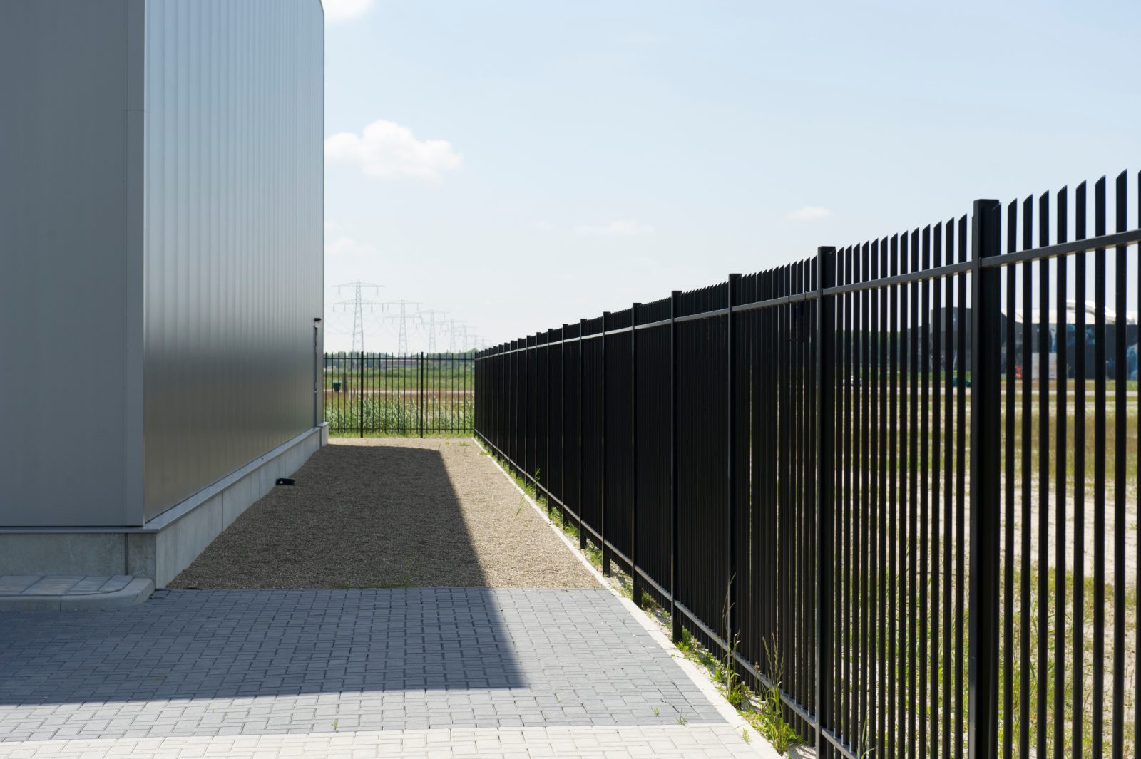 Zwart hekwerk langs een gebouw met grindpad